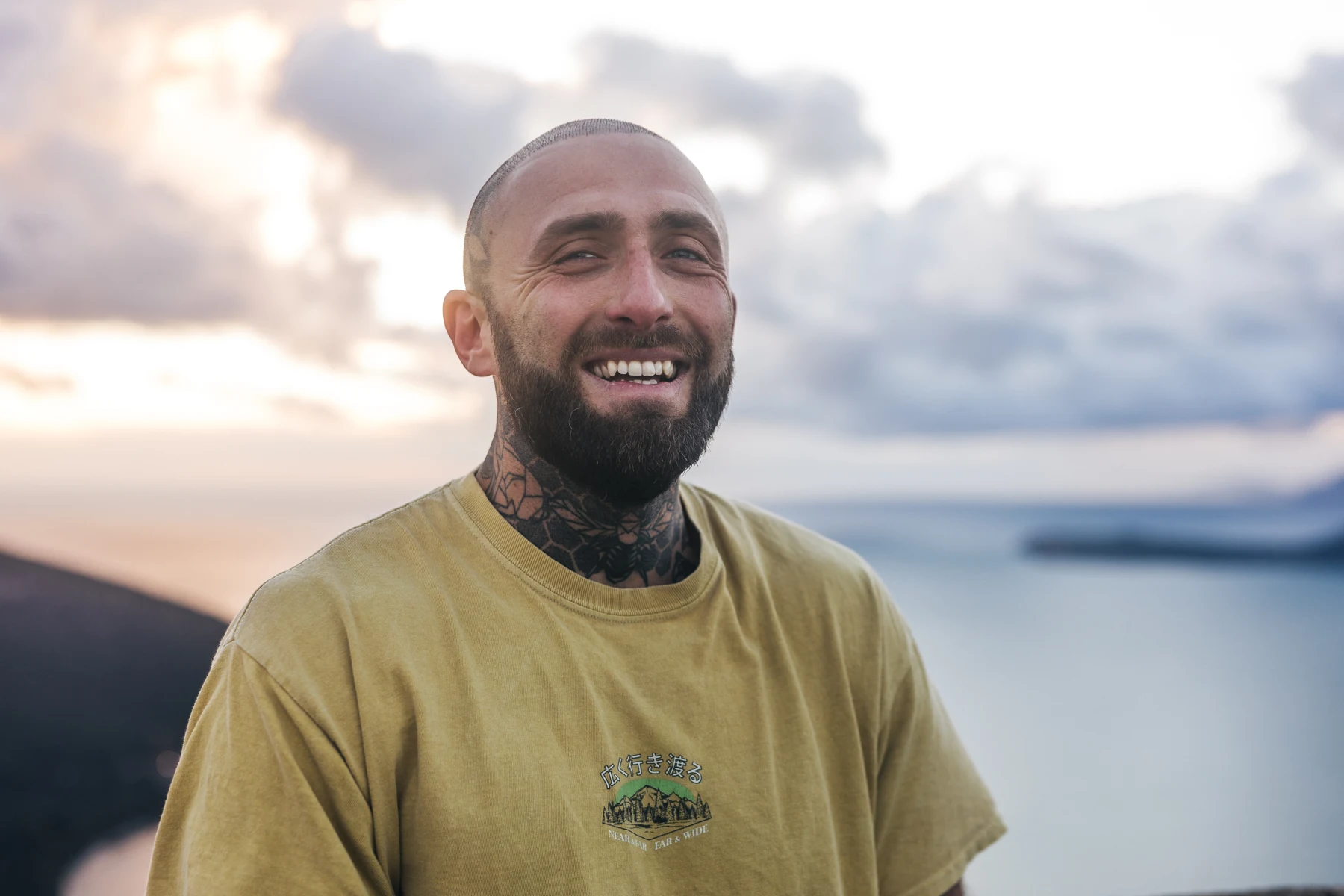 Aaron Parker with a shaved head, wearing a yellow T-shirt by the sea