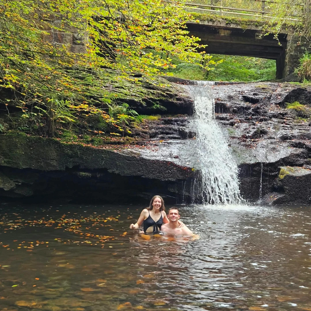 Two people in a woodland pool beneath a waterfall, from The Conscious Self’s published Facebook post